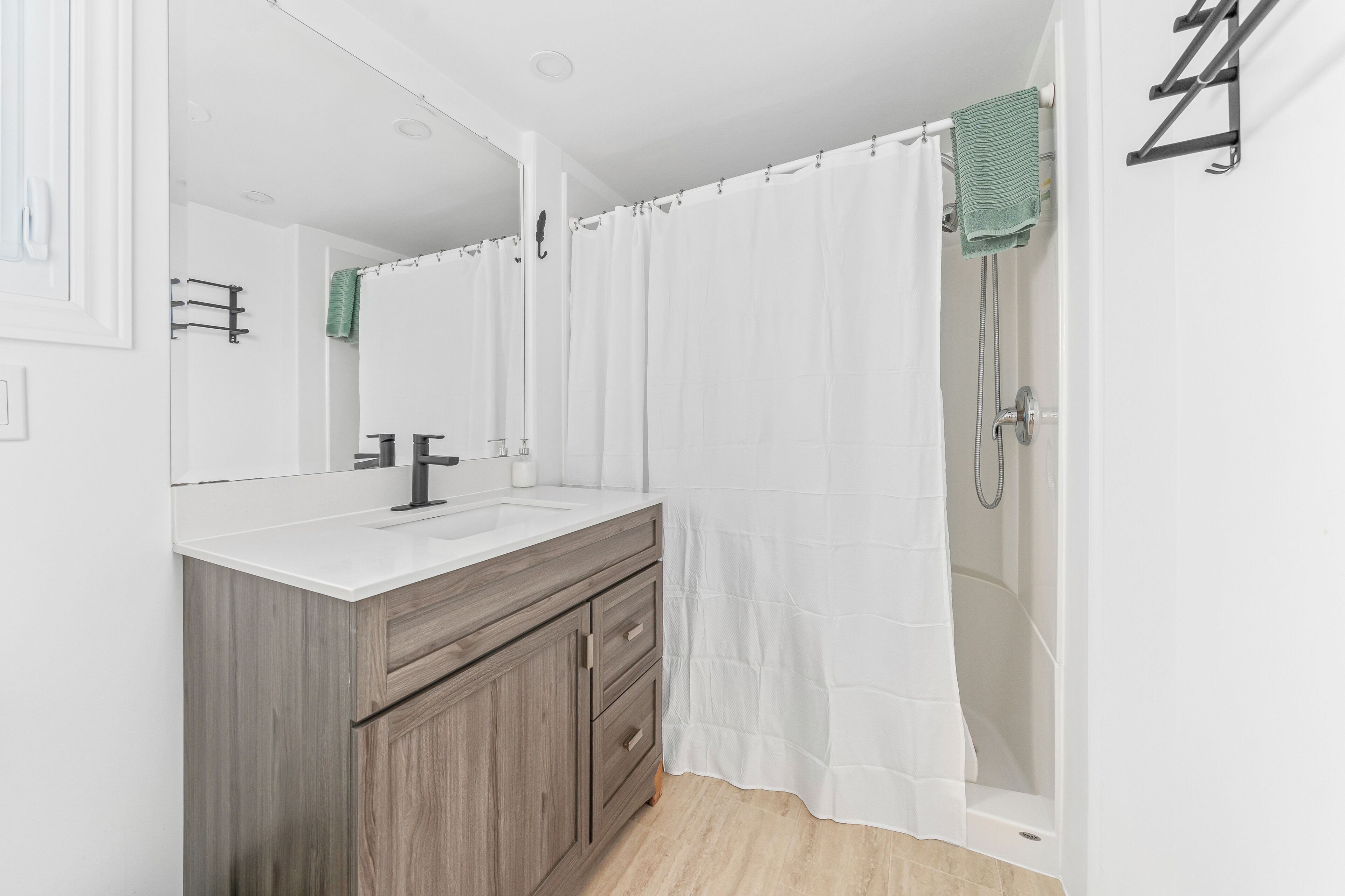 A modern bathroom with a wooden vanity, a white sink, and a shower with a white curtain.