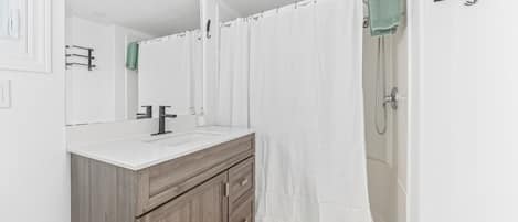 A modern bathroom with a wooden vanity, a white sink, and a shower with a white curtain.