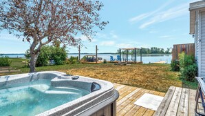 A hot tub on a wooden deck with a view of a lake and a wooden fence in the background. - The Birch (Prince Edward)
