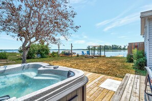 Un jacuzzi en una terraza de madera con vista a un lago y una valla de madera al fondo.