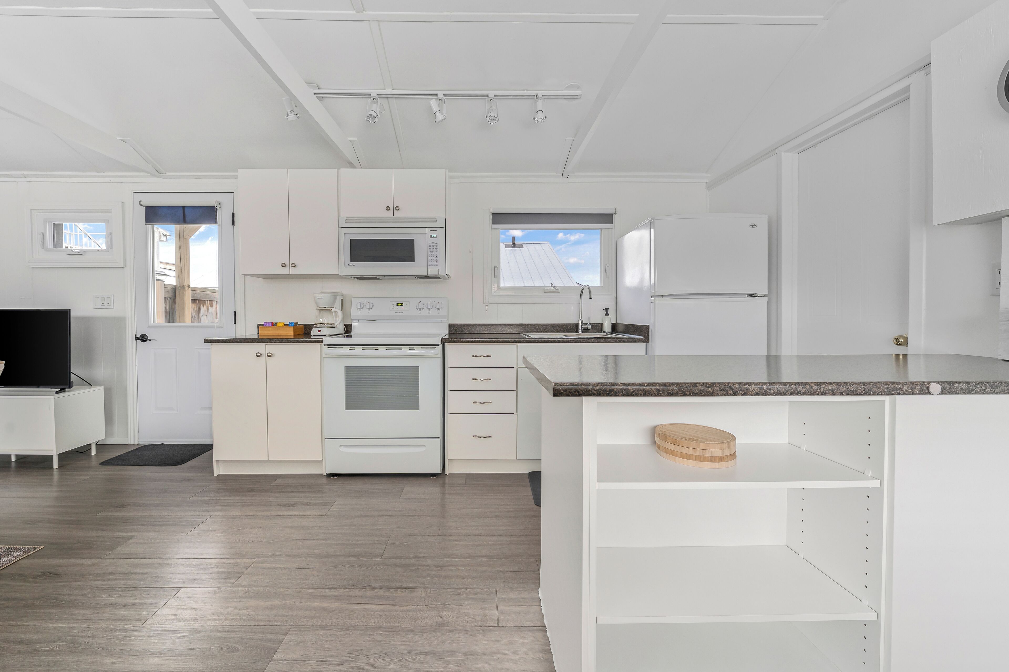 A modern kitchen with white cabinetry, a built-in microwave, oven, and refrigerator. There is a small island with a cutting board and a sink.