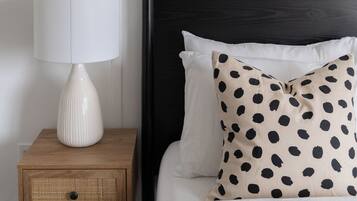 Een keurig opgemaakte slaapkamer met een bed, een bedlampje, een klein houten nachtkastje en twee ingelijste foto’s aan de muur.