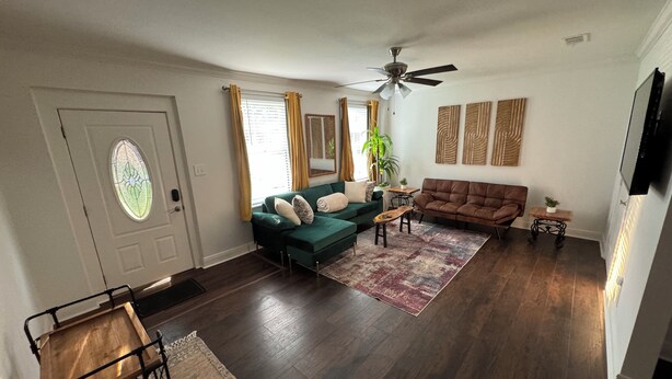Ein Wohnzimmer mit einem grünen Sofa, einem braunen Sofa, einem Deckenventilator und einem Couchtisch aus Holz.