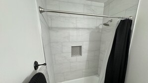 Ein Badezimmer mit einer weißen Badewanne, einer Dusche mit Glastür und einem Handtuchhalter mit Handtuch.