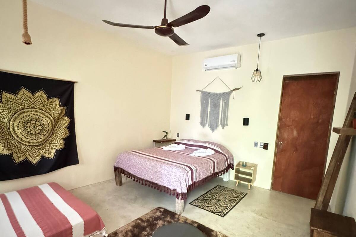 A bedroom with a bed, a chair, a ceiling fan, a wall-mounted air conditioner, and a door.
