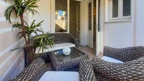 A cozy outdoor seating area with patterned cushions and a small table, surrounded by a potted plant and a door leading to another room.