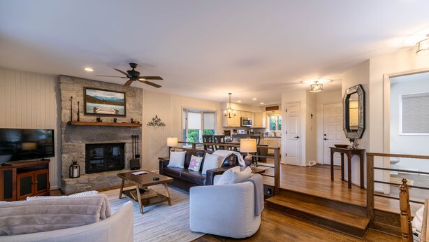 A spacious living room with a fireplace, a television, and a dining area with a kitchen in the background.
