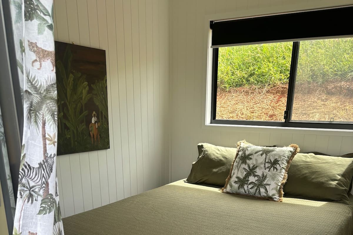 A bedroom with a bed, pillows, a window, and a curtain.