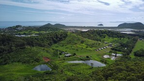 A lush green landscape with a small pond, a few buildings, and a distant view of the sea. - High Valley Dawn Permaculture Farm (Lammermoor)
