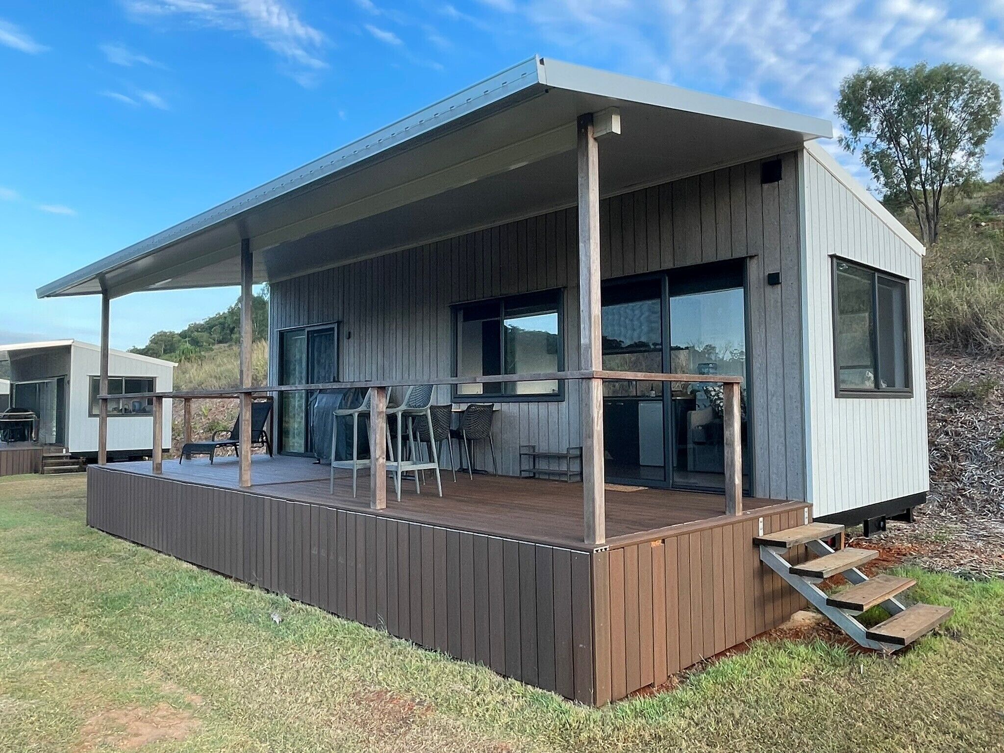 Une maison moderne dotée d’une terrasse en bois, de grandes fenêtres et d’un patio couvert.