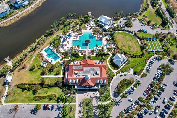 An aerial view of a resort with multiple swimming pools, a large central building, and a parking area.
