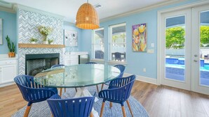 A modern kitchen with a glass dining table, blue chairs, and a hanging light fixture.