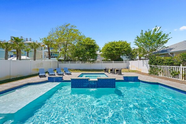 Una piscina con acqua cristallina e blu, circondata da sdraio e una recinzione bianca.
