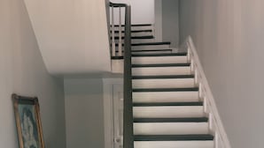 A staircase with white steps and dark railings, leading to a landing with a framed picture and a small table with a candle.