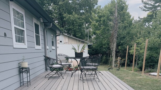 A wooden deck with a table and chairs, surrounded by a house and greenery.