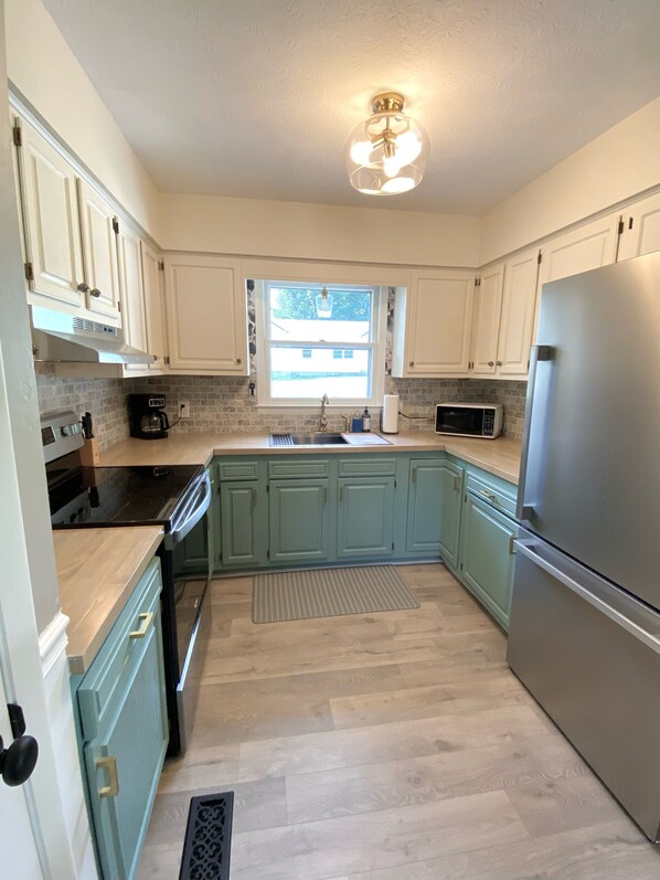 A modern kitchen with light green cabinets, stainless steel appliances, a double sink, and a window providing natural light.