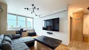 A modern living room with a large sectional sofa, a flat-screen TV mounted on the wall, and a wooden floor.