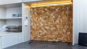 A wall with a corkboard design, a desk with a computer, and a shelf with a tissue box and a basket.
