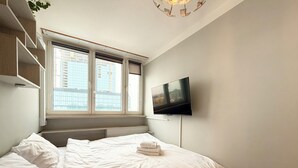 A bedroom with a bed, a TV mounted on the wall, and a window with blinds.
