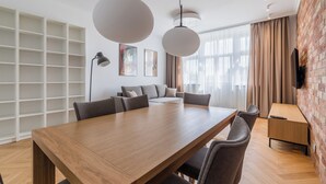 A modern living room with a wooden dining table, grey sofas, and a brick accent wall. - Kochanowskiego Luxury Apartment (Poznań)