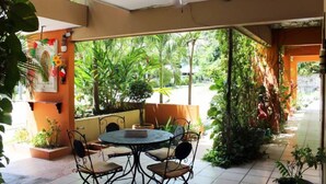 Een terras buiten met een ronde tafel en stoelen, omgeven door weelderige begroeiing en planten.
