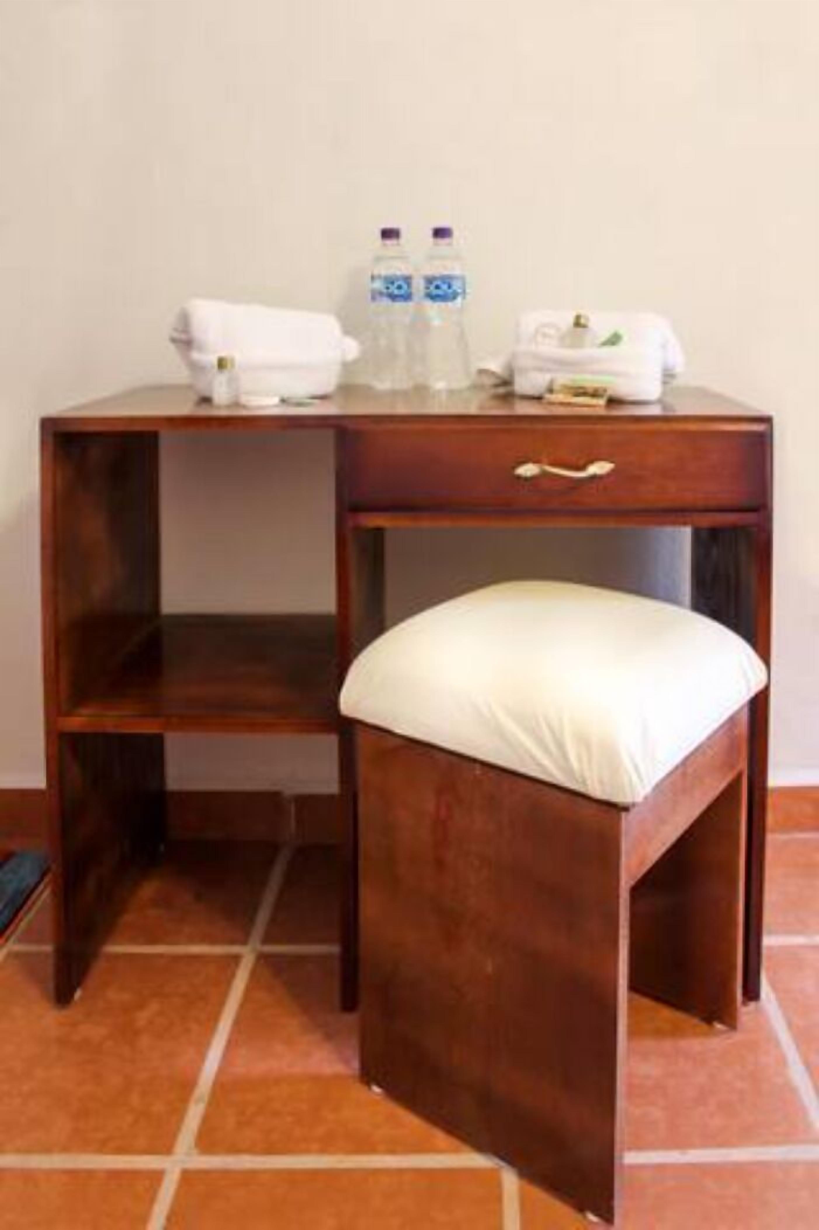 Un bureau en bois avec un tiroir, un petit tabouret et une bouteille d’eau posée dessus.
