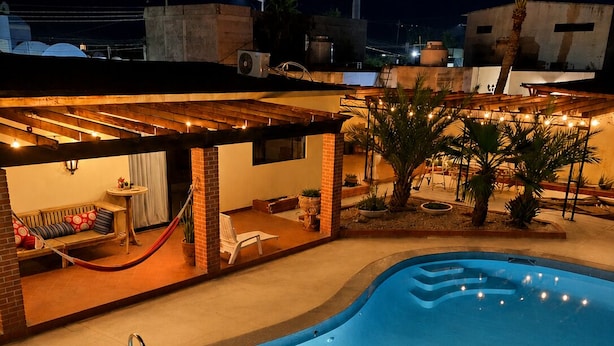 Une piscine avec une terrasse en bois, un hamac et un petit coin salon agrémenté de coussins.