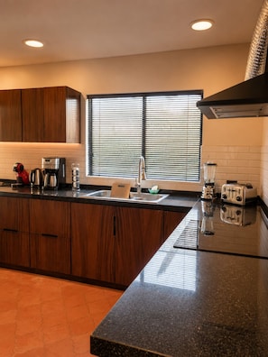 A modern kitchen with wooden cabinets, a black countertop, a window with blinds, and a toaster.