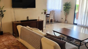 A living room with a sofa, a coffee table, a TV, and a dining area with a table and chairs.