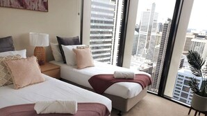 Une chambre d’hôtel avec deux lits, une grande fenêtre donnant sur la ville, une plante en pot et une lampe.