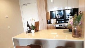 Une cuisine moderne avec un îlot central, deux chaises marron, une bouteille de vin et une plante en pot.
