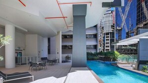 An indoor swimming pool area with a modern pool, seating, and a view of a building under construction.