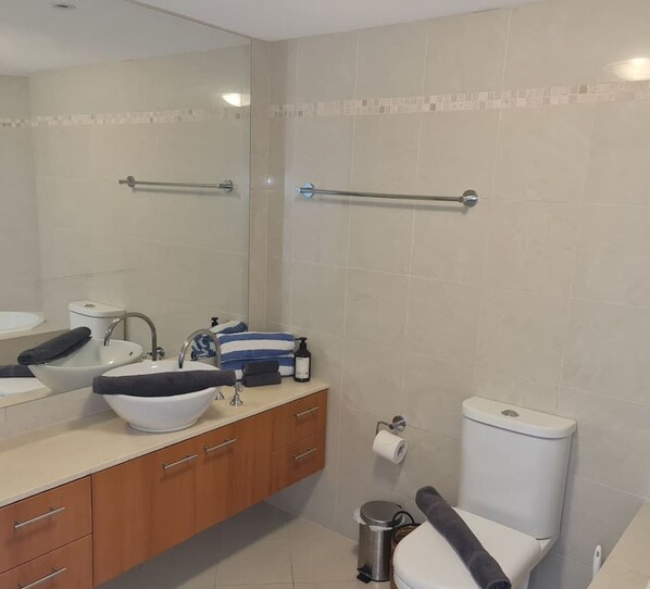 Un baño moderno con dos lavamanos, un inodoro y un cubo de basura.