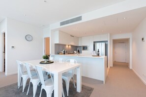 Une cuisine moderne avec des meubles blancs, un îlot central et un coin repas avec des chaises blanches.