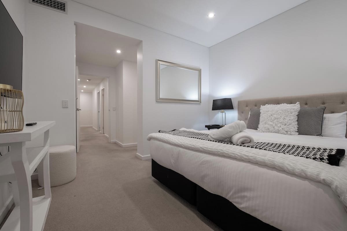 A modern bedroom with a large bed, a bedside table, a lamp, and a mirror.