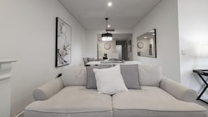 Un salon moderne avec un canapé beige, un lustre et un coin repas à l’arrière-plan.