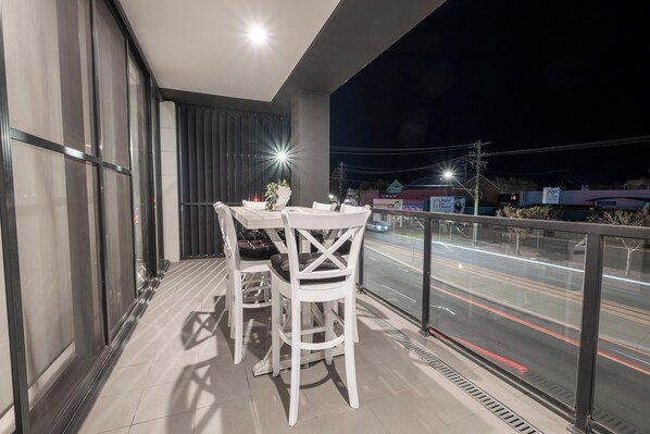 A balcony with a table and chairs, a potted plant, and a view of a road with light trails.