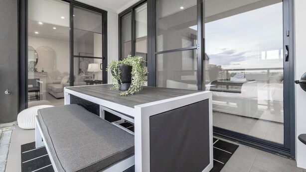 Une chambre moderne dotée d’une grande porte-fenêtre coulissante donnant sur un balcon, d’une petite table avec une plante et d’un banc.