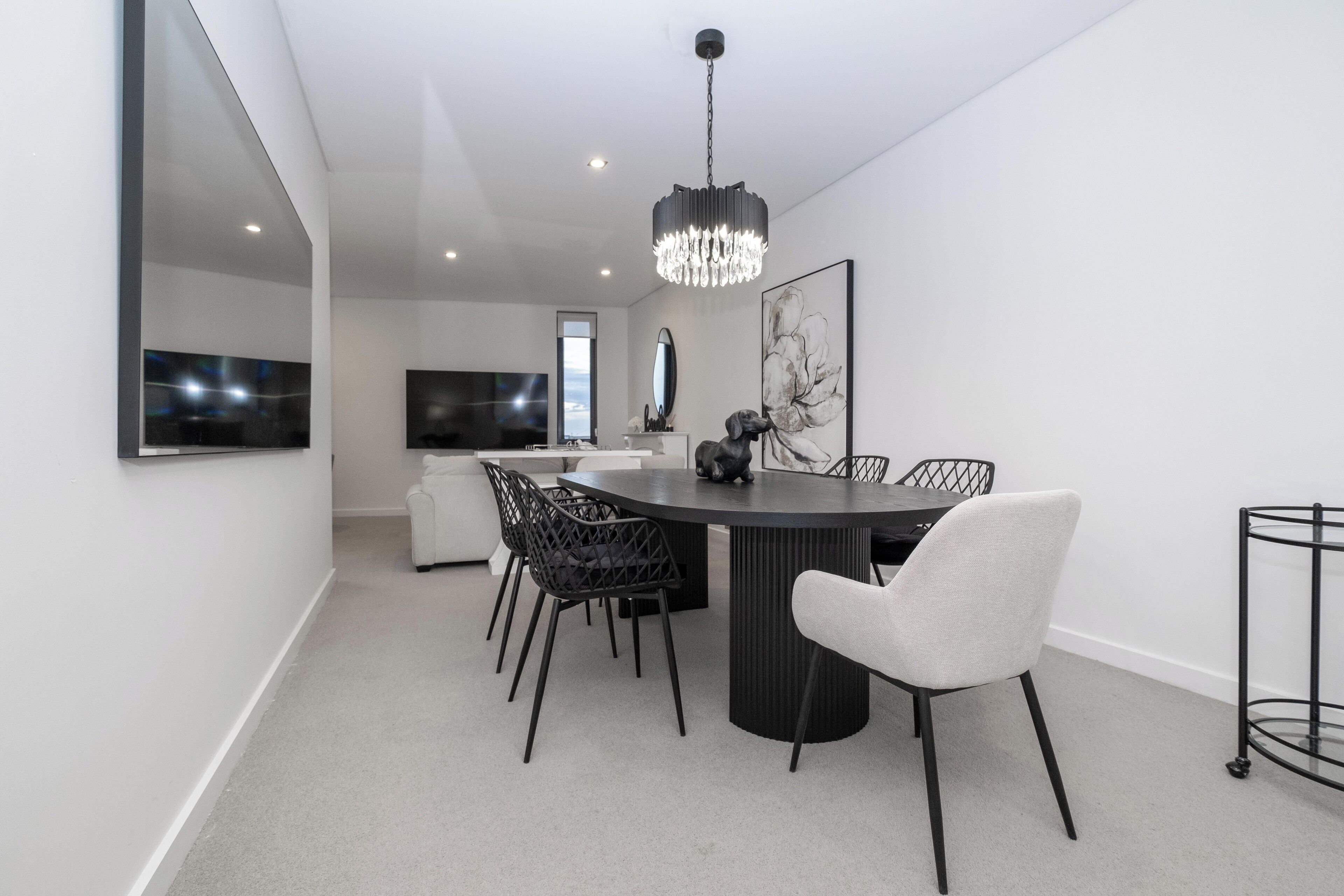 A modern dining area with a round table, black chairs, a chandelier, and a large mirror on the wall.