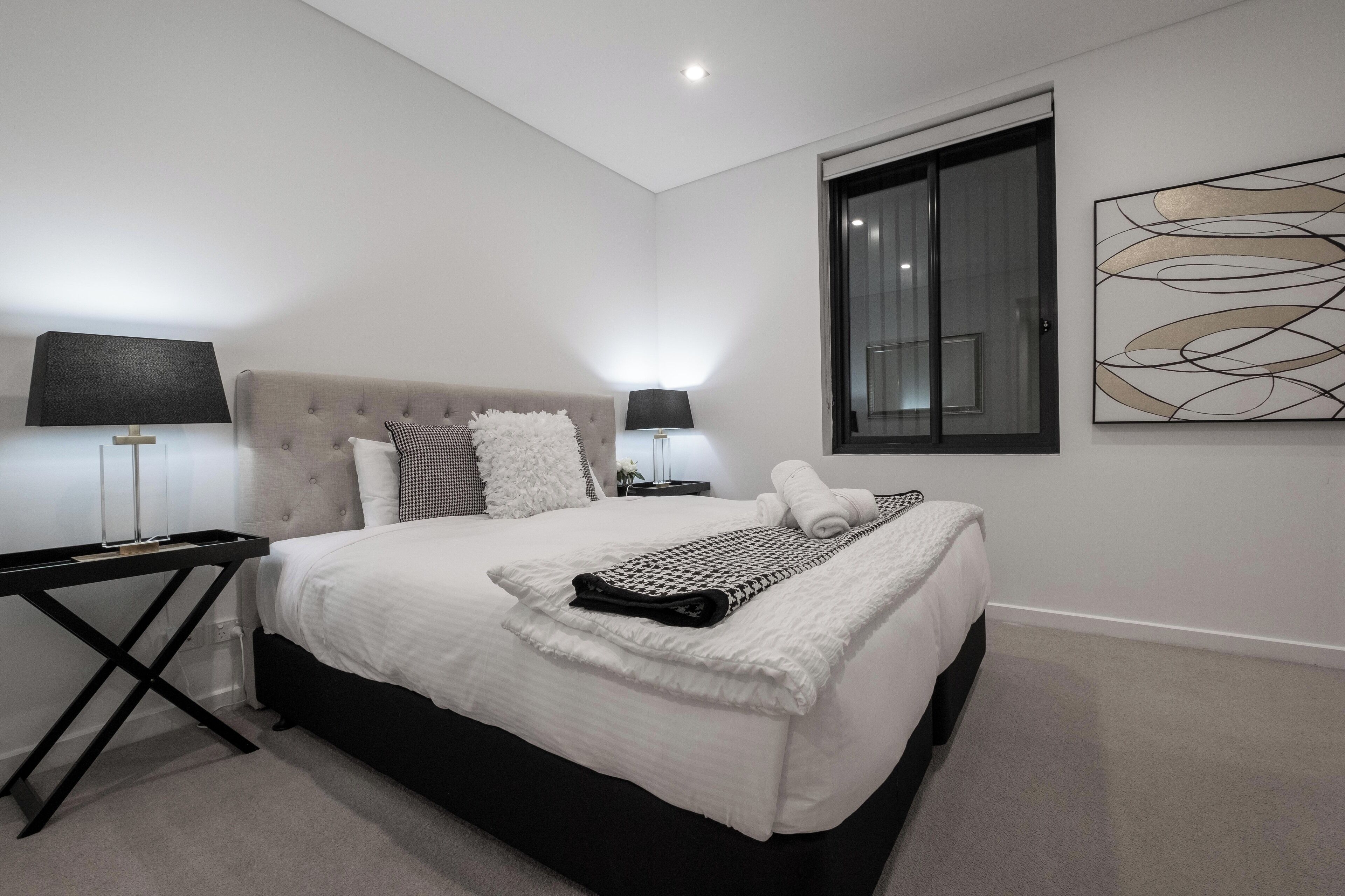 Un dormitorio moderno con una cama grande, una mesita de noche, una lámpara y una ventana con persianas.