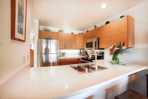 A modern kitchen with stainless steel appliances, wooden cabinets, and a white countertop.