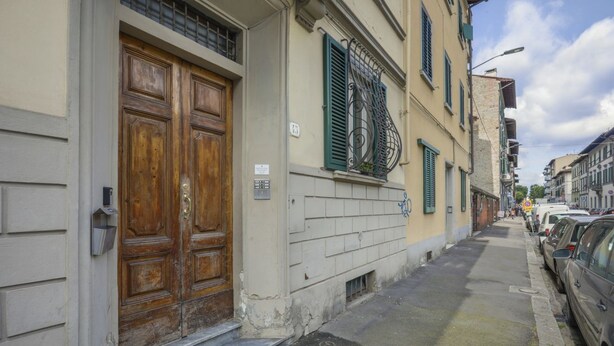 A narrow street with parked cars, a wooden double door, and a building with a balcony. - Angelico's Urban Loft (Firenze)
