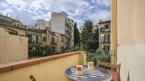 A balcony with a round table and two chairs, overlooking a residential area with buildings and trees. - Angelico's Urban Loft (Firenze)