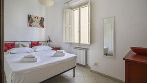 A bedroom with a bed, a window, a radiator, a mirror, and a red cabinet. - Angelico's Urban Loft (Firenze)