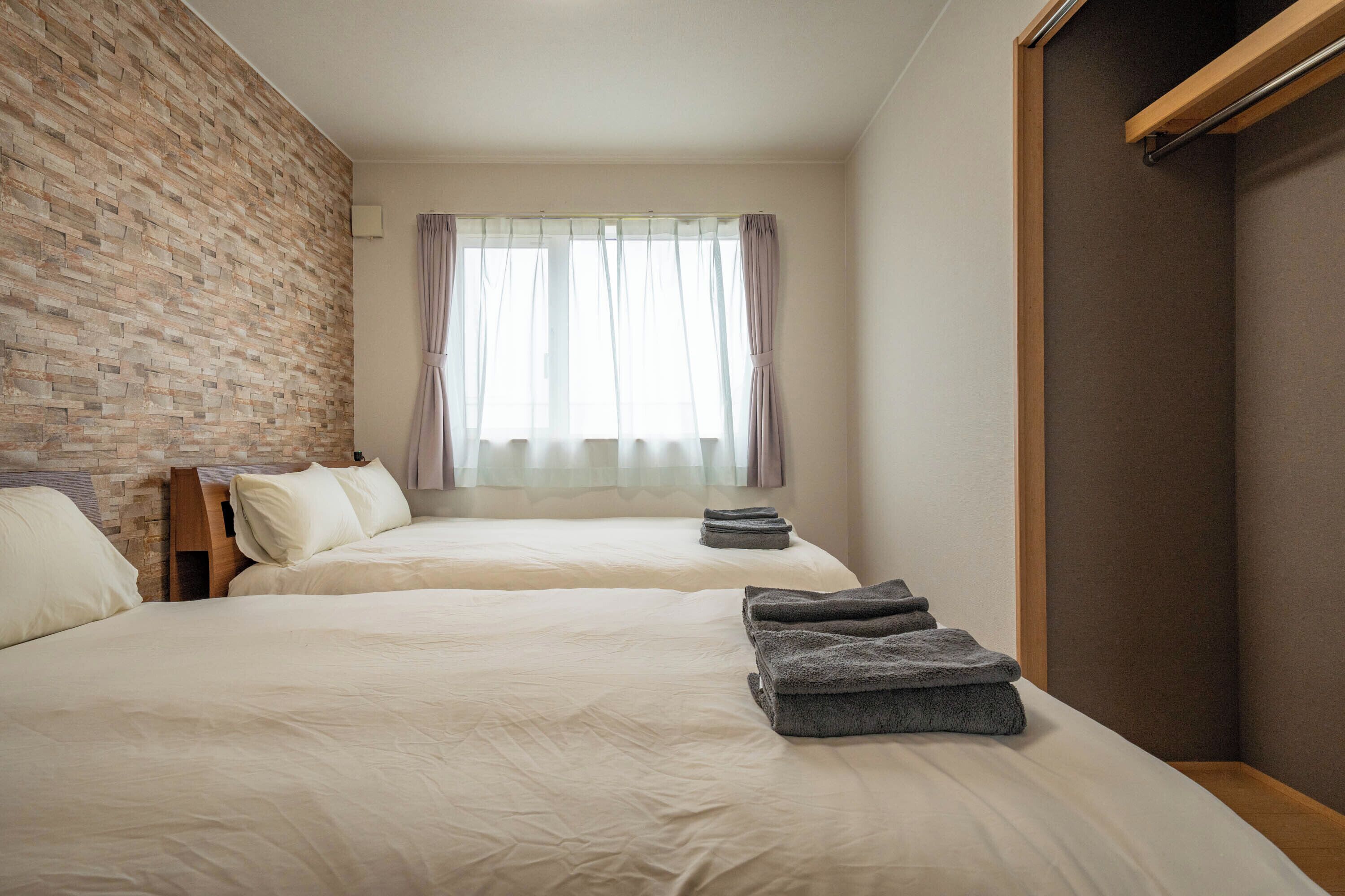 Habitación de hotel con dos camas, una pared de acento de ladrillo, una ventana con cortinas traslúcidas y un armario de madera.
