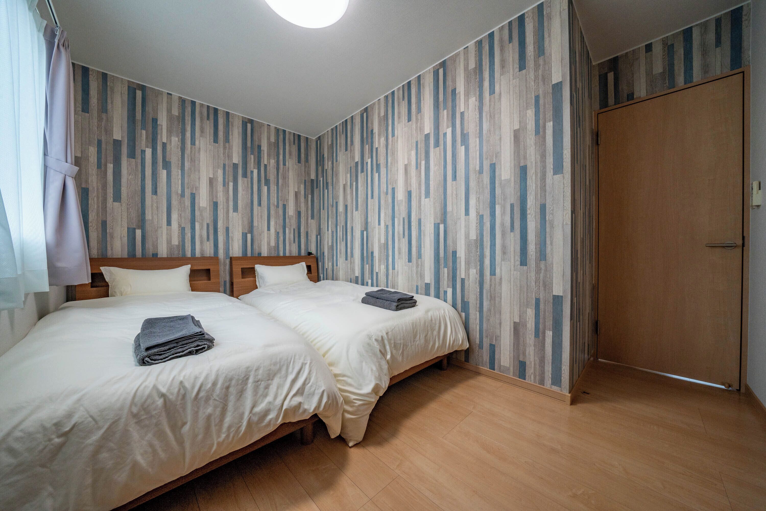 A bedroom with two beds, wooden flooring, and a wooden door.