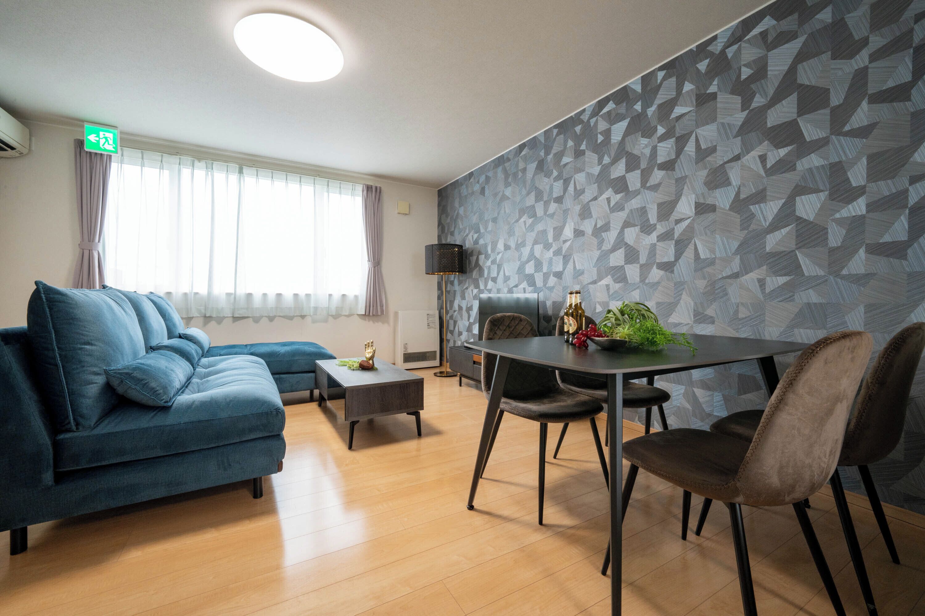 A modern living room with a sofa, a dining table with chairs, a lamp, and a geometric-patterned wall.
