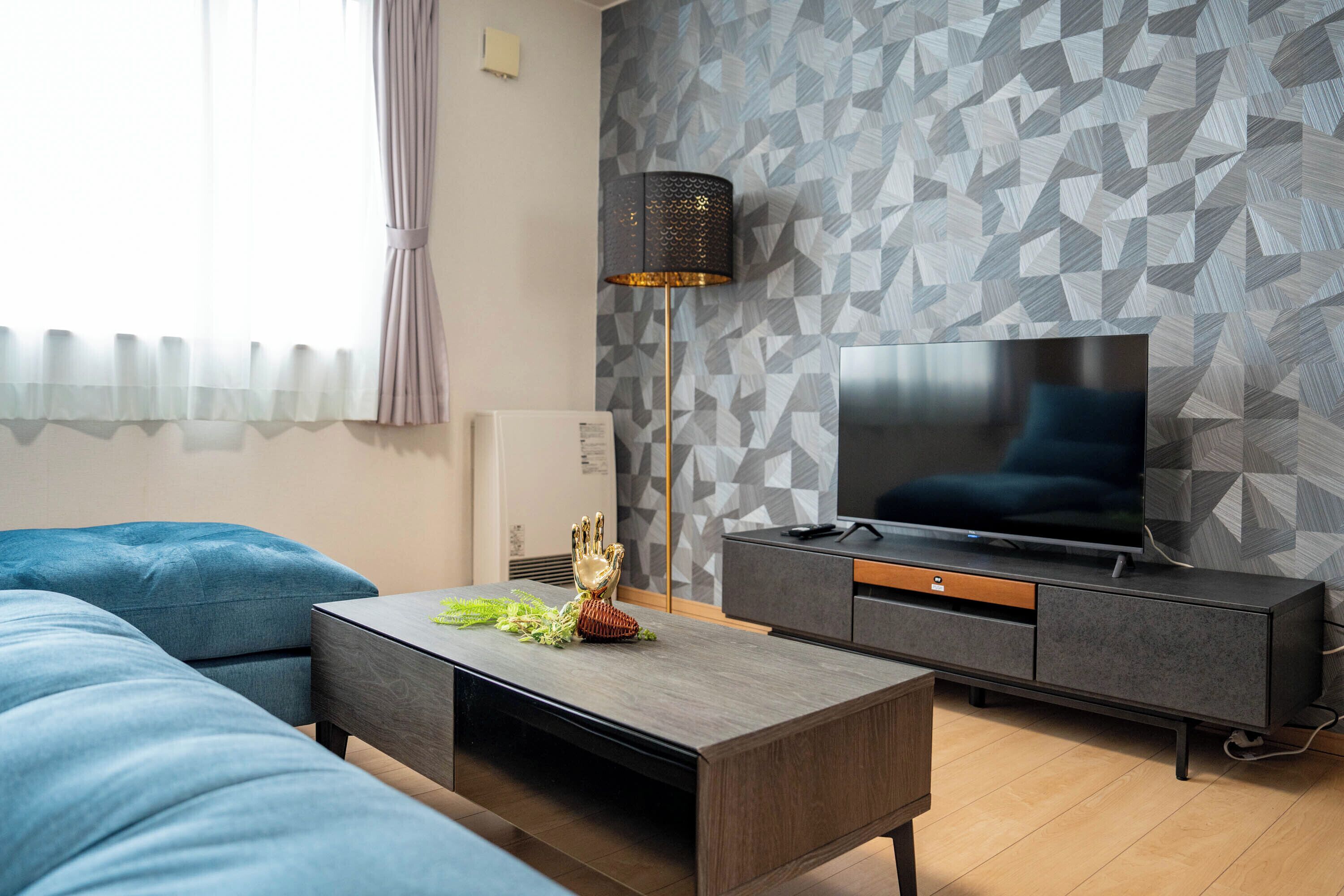 A modern living room with a sofa, coffee table, TV, and patterned wall.