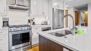 A modern kitchen with stainless steel appliances, white cabinetry, and a marble countertop.