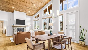 A spacious living area with a fireplace, wooden ceiling, and large windows.